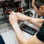 An electrician uses a multimeter to test and diagnose connections in an open electrical panel.